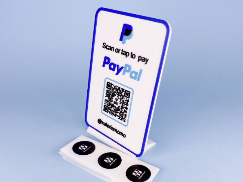 Hvitt bordskilt med blå ramme, QR-kode, NFC-symboler og eksempel på betalingsprofil